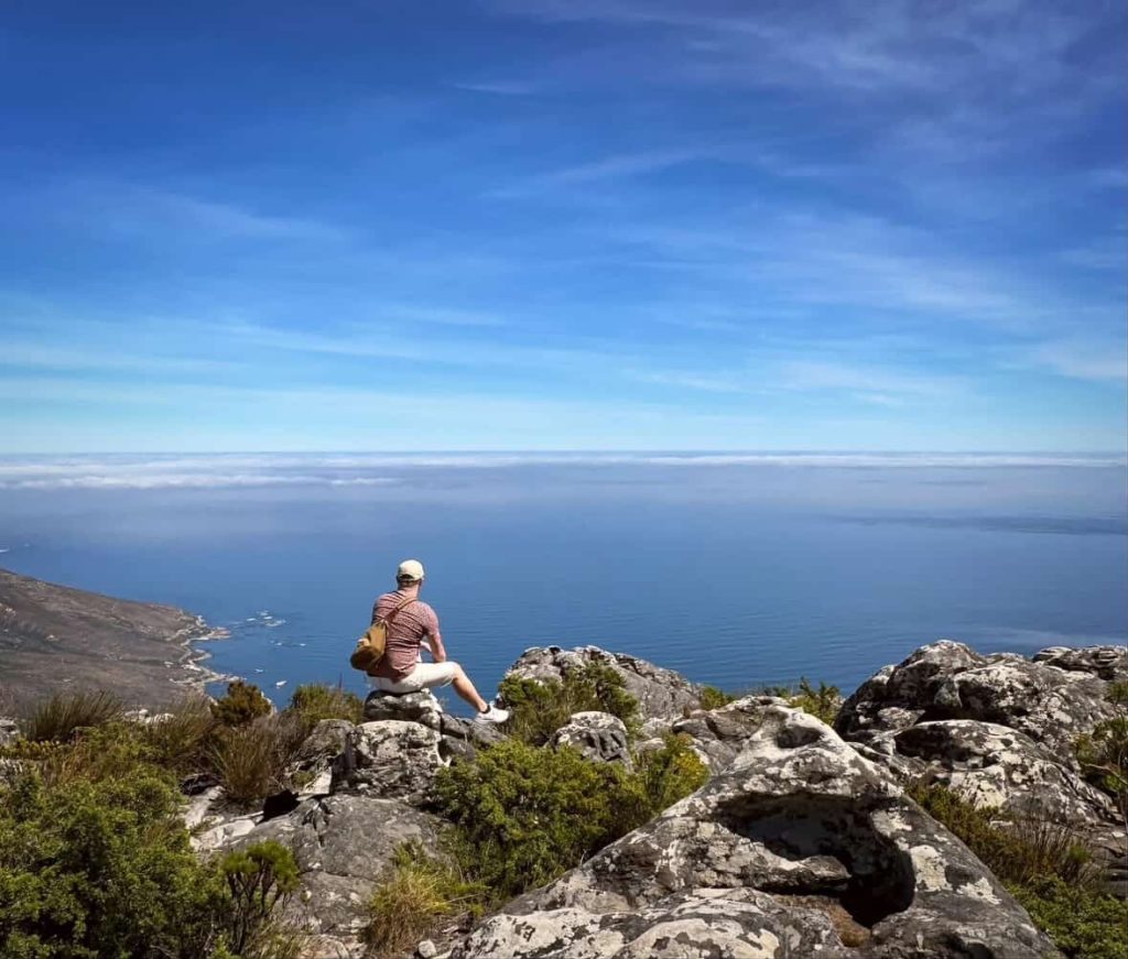 Man sits on rocks overlooking the ocean from a mountain in Cape Town.