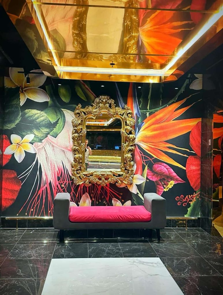 Luxurious lounge area in Cape Town with tropical floral wallpaper, gold mirror, and pink bench