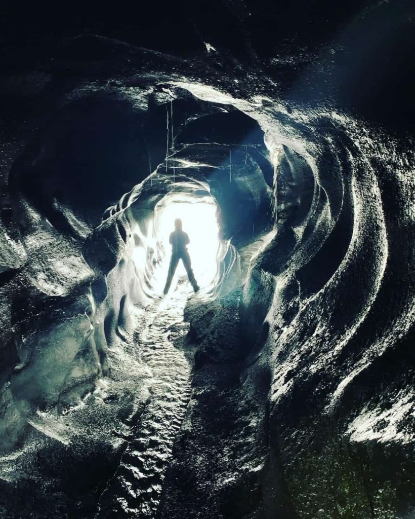 Person silhouetted in a bright Reykjavik ice cave tunnel with textured walls.
