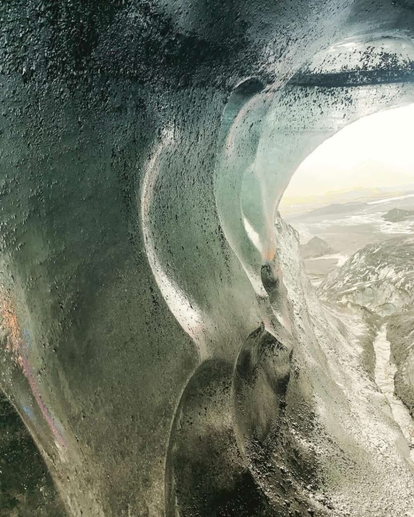 Ice cave interior in Reykjavik, Iceland, with glacial formations and a distant view of a snowy landscape.