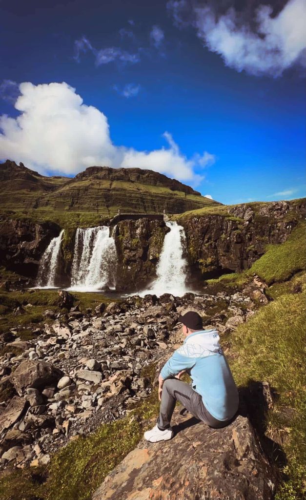 Man sits contemplating Kirkjufellsfoss waterfall near Reykjavik, Iceland.