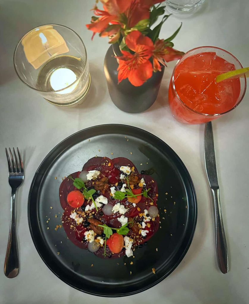 Beetroot carpaccio with goat cheese, nuts, and berries, served with a red drink in Cape Town.