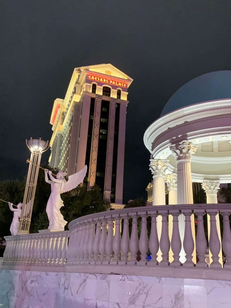 Caesars Palace at night in Las Vegas, with angel statues and Roman architecture.