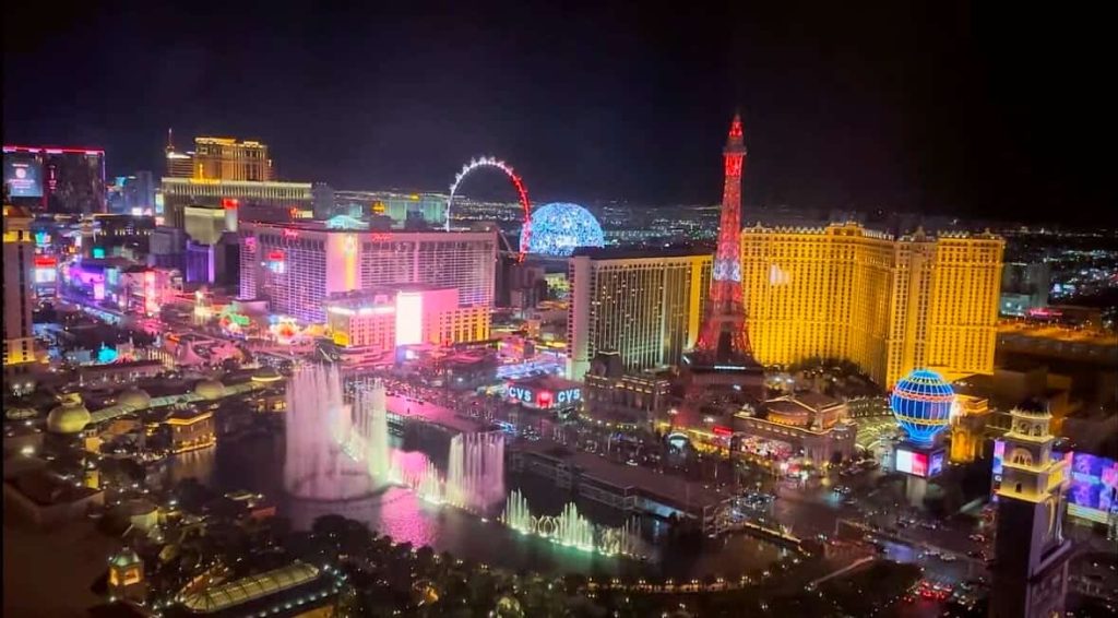Las Vegas Strip at night, illuminated hotels, Bellagio fountains, and High Roller observation wheel.