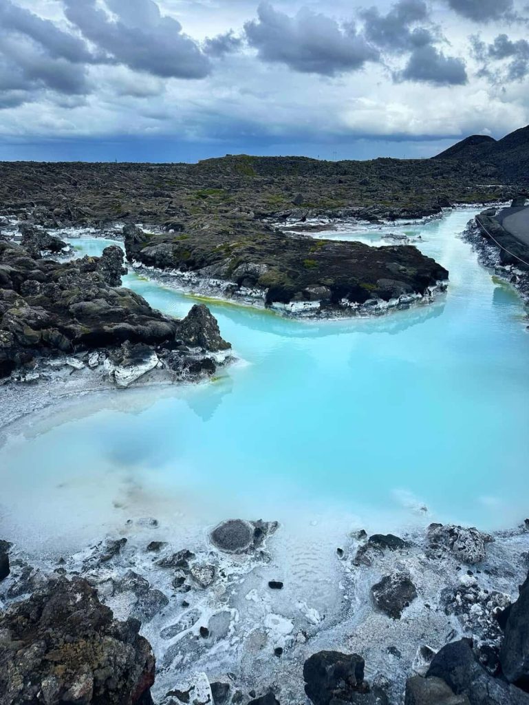 Milky blue water winds through black lava rocks under a cloudy sky in Reykjavik.
