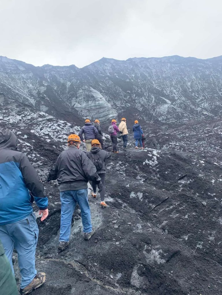 Hikers with helmets trek across a black glacier near Reykjavik.