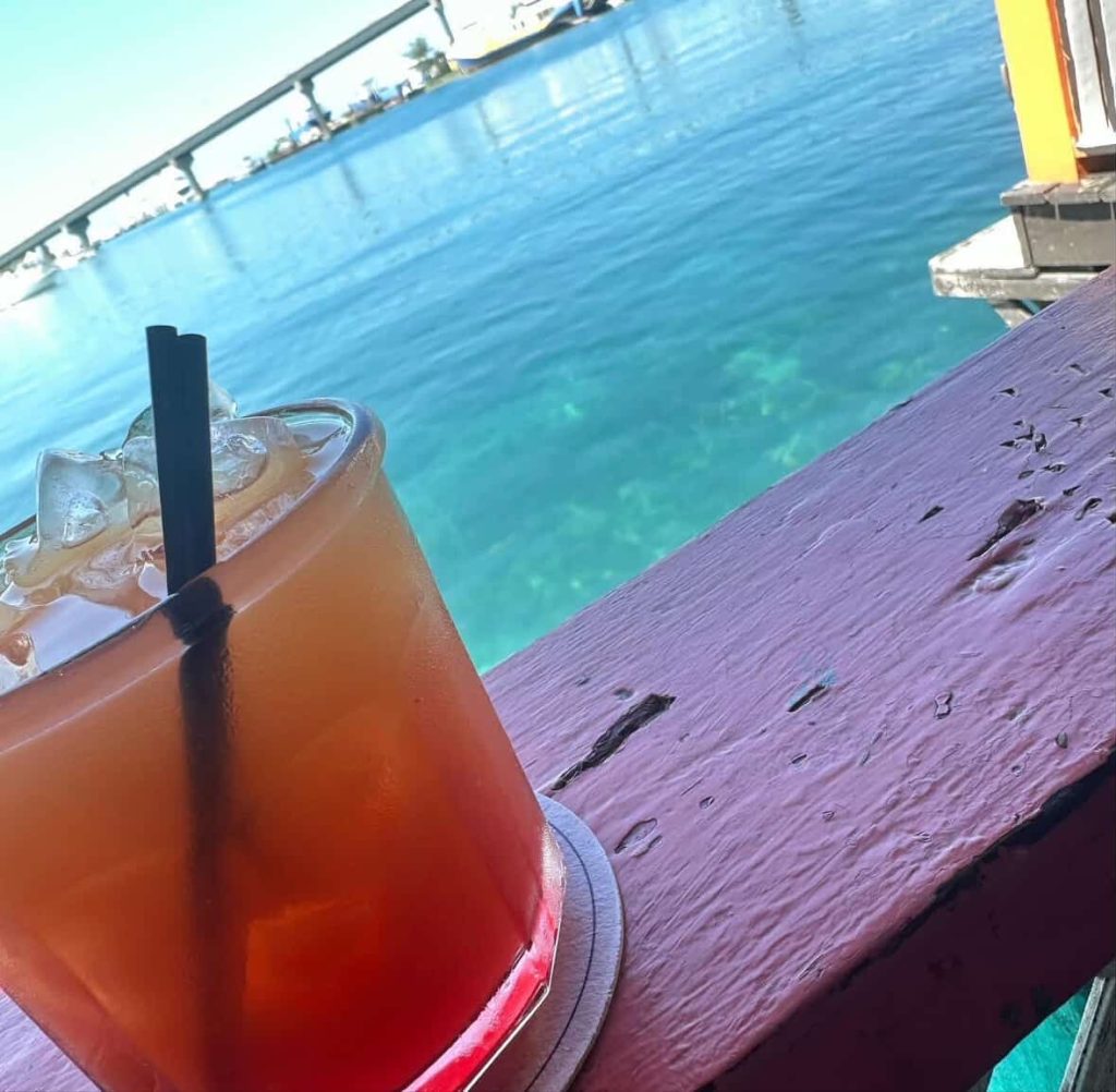 Nassau cocktail on a weathered railing overlooking turquoise water and a bridge.