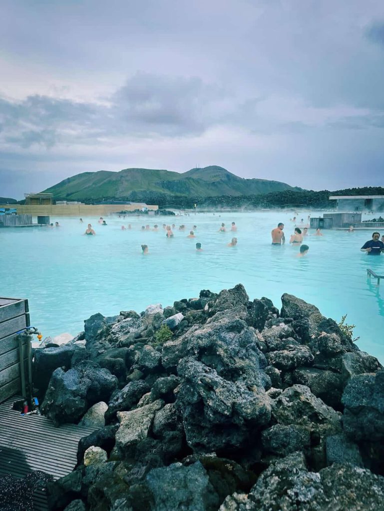 People bathing in the milky blue waters of the Blue Lagoon, Iceland, with mountains in the background.