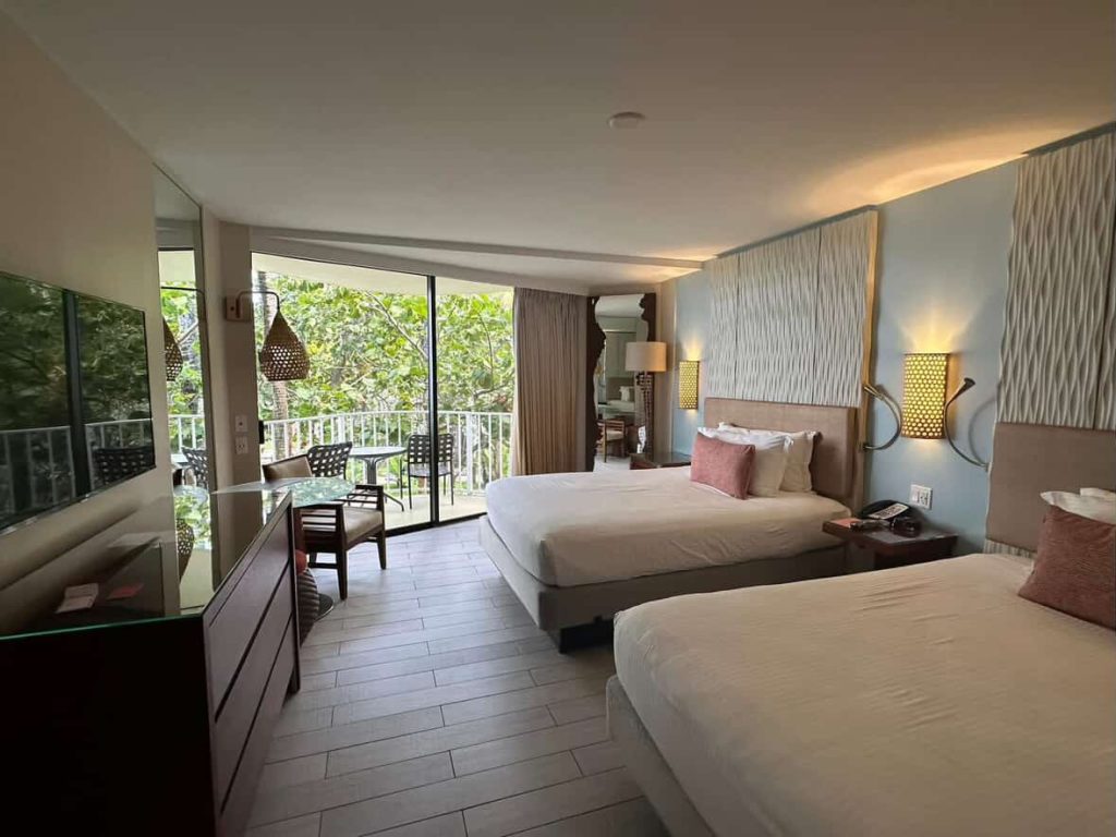 Hotel room in Nassau with two beds and a balcony overlooking lush greenery.