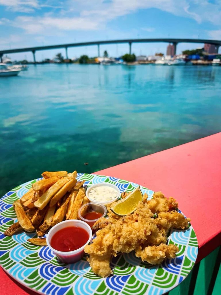 Fried fish, fries, and dipping sauces on a plate with Nassau harbor in background
