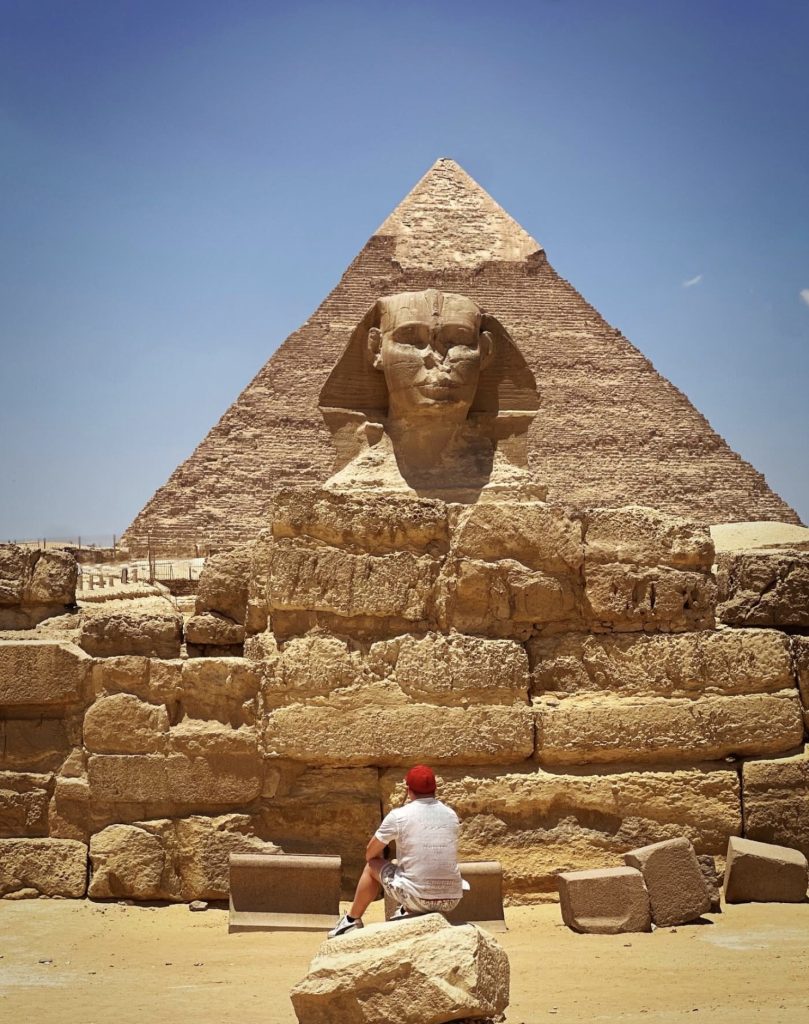 Man sits before the Sphinx and a pyramid in Giza, Egypt. Ancient Egyptian history.
