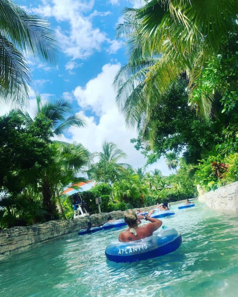 People relax on tubes in a lazy river at Atlantis, Nassau, under palm trees.