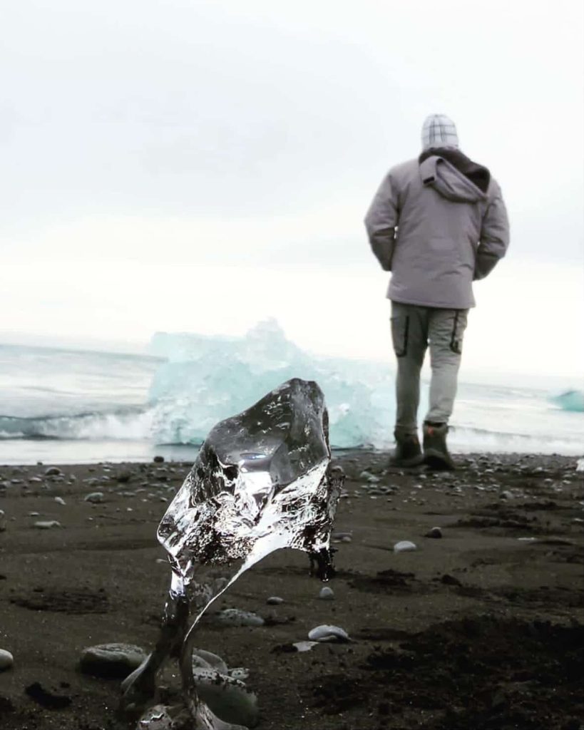 Ice on black sand beach near Reykjavik, Iceland, with a person walking toward the ocean.