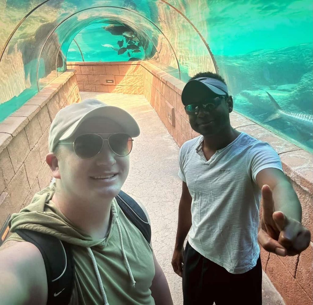 Two men smile in a clear underwater tunnel aquarium in Nassau.