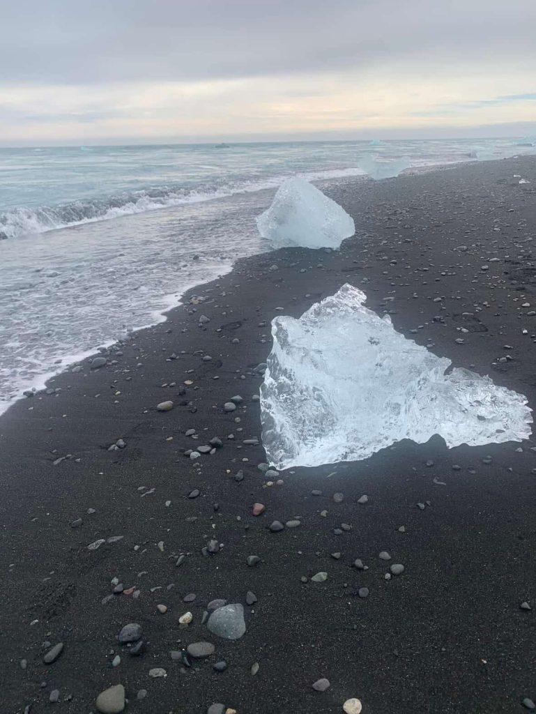 Icebergs on a black sand beach near Reykjavik, Iceland. Waves gently lap the shore.