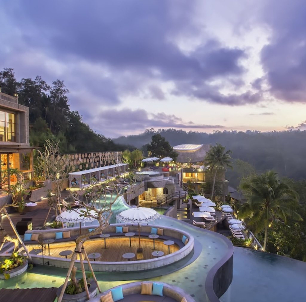 Luxury Bali resort at dusk with infinity pool and lush jungle views.
