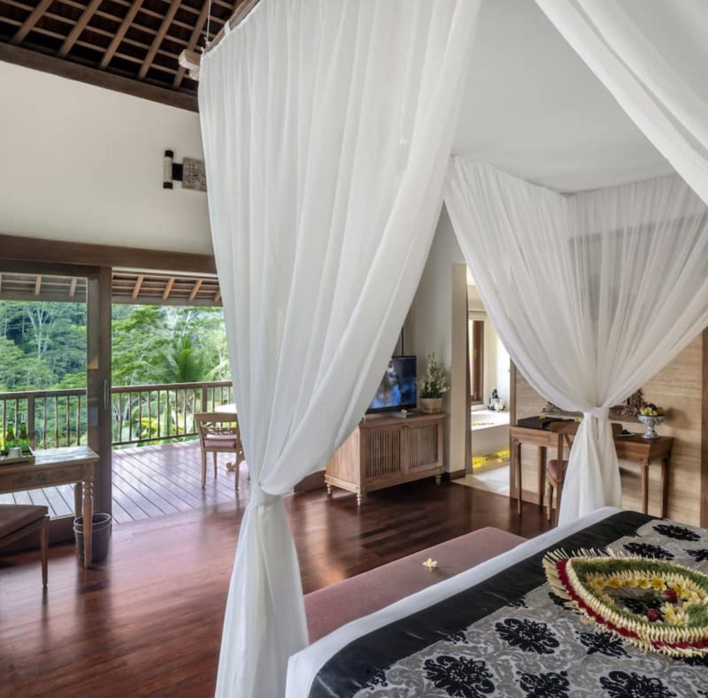Luxurious Bali bedroom with canopy bed, balcony view of lush greenery.