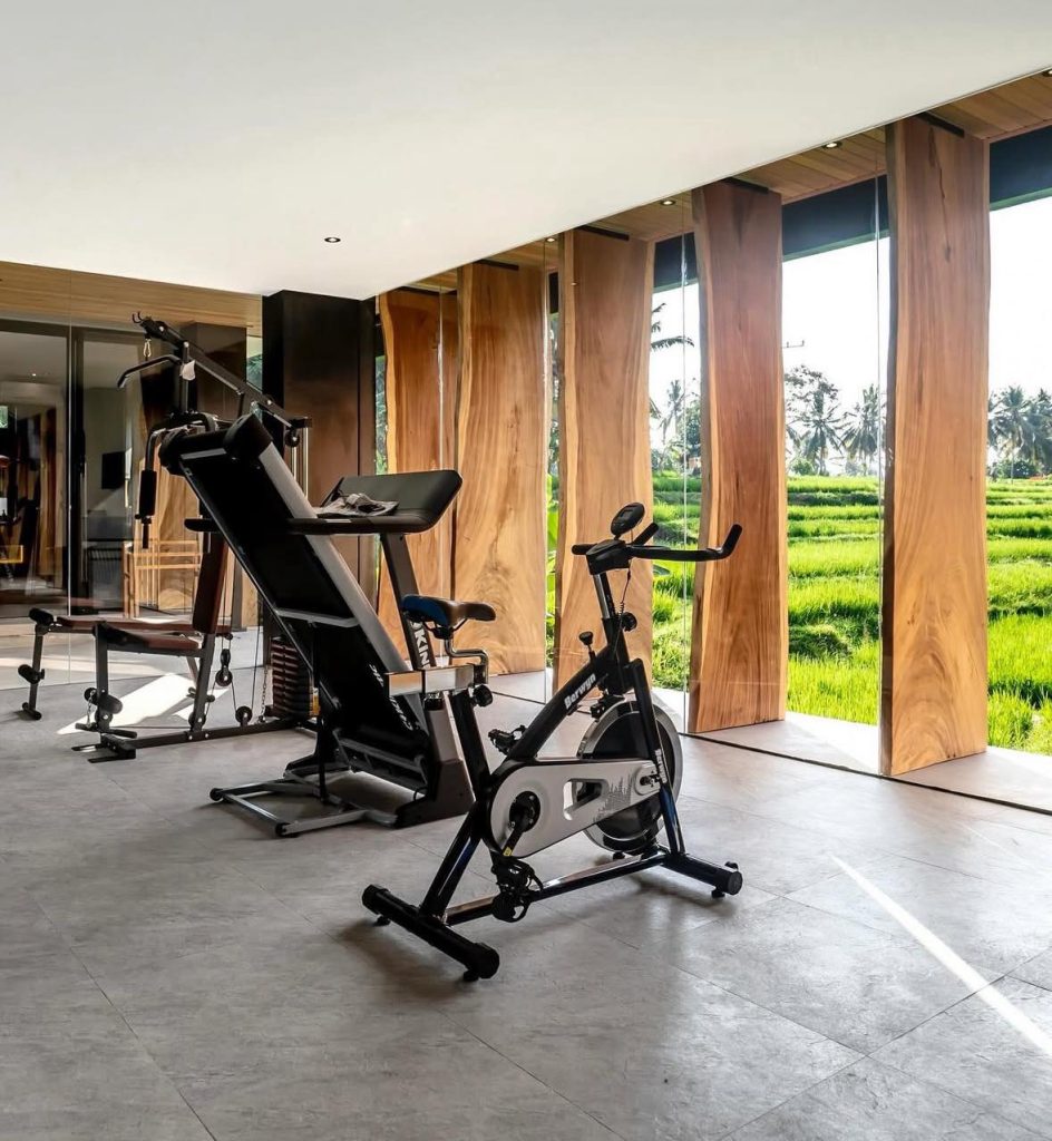 Home gym with exercise bike and weight machine overlooking Bali rice fields