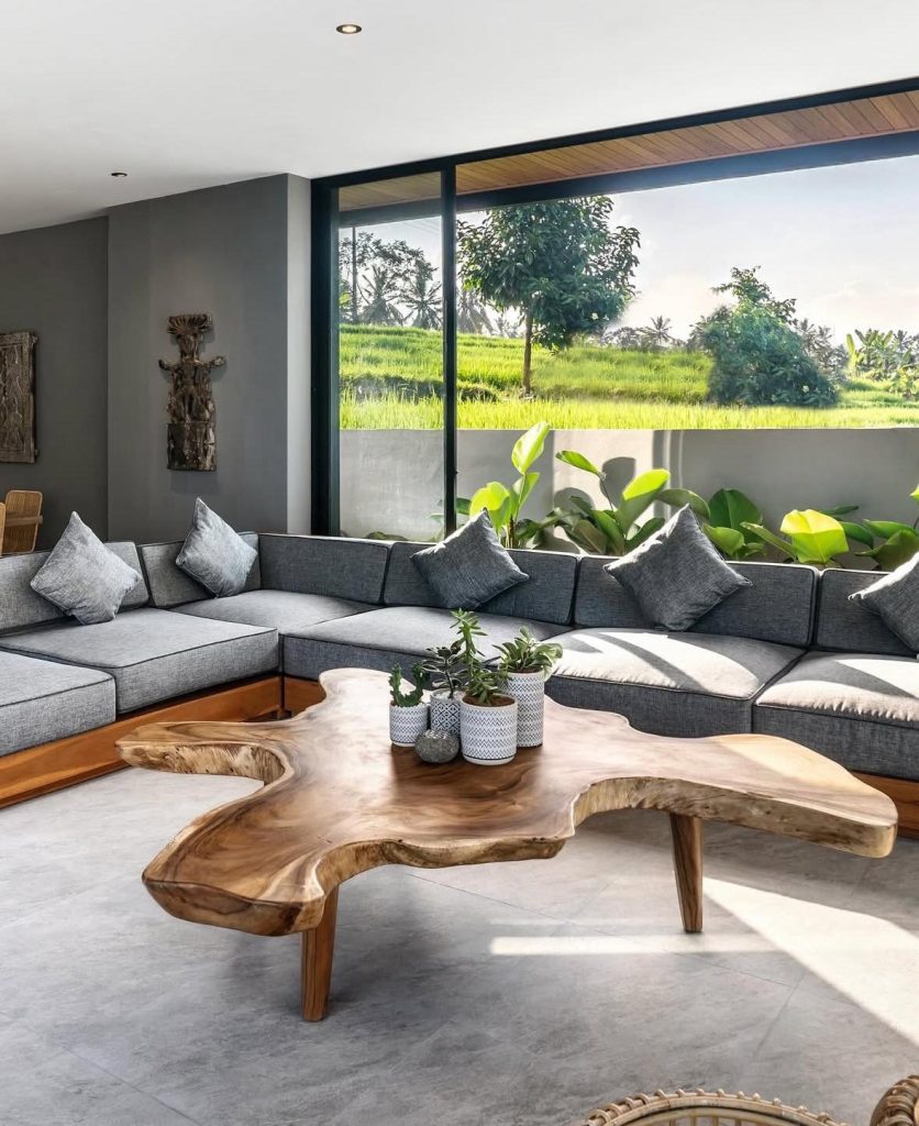Modern living room in Bali with large sectional sofa and live-edge coffee table overlooking rice paddies.