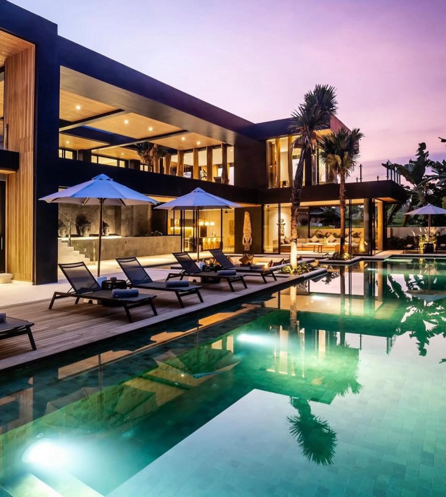 Luxury Bali villa with infinity pool at sunset, featuring modern architecture and palm trees.