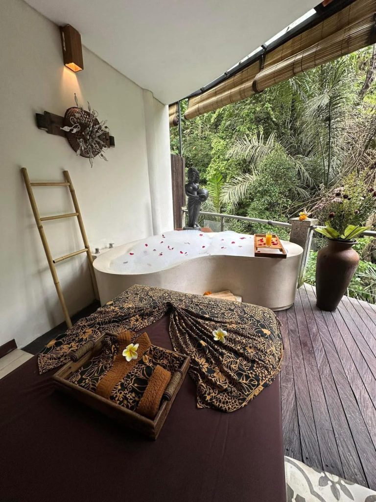 Luxury Bali spa bathroom with soaking tub, lush jungle view, and massage bed.