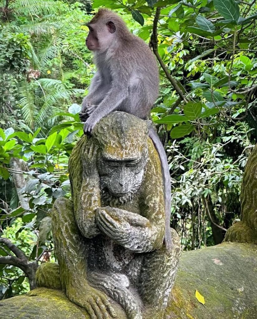 Monkey sitting on stone monkey statue in lush Bali jungle