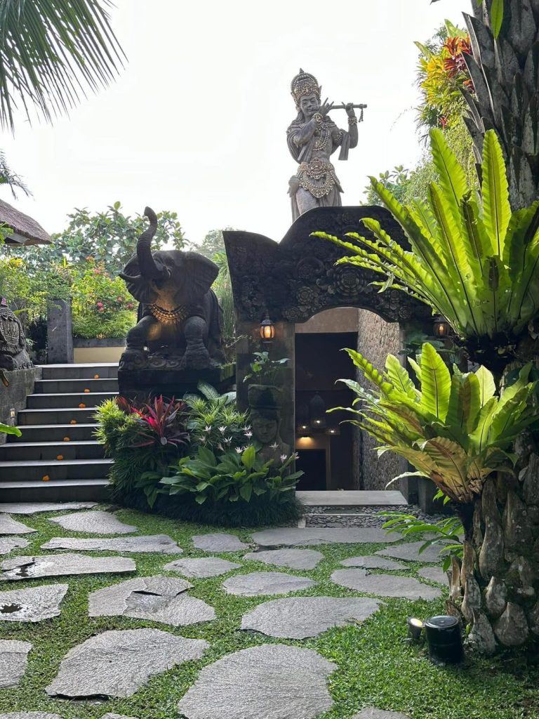 Stone elephant statue leading to an arched entryway in Bali, with lush greenery.