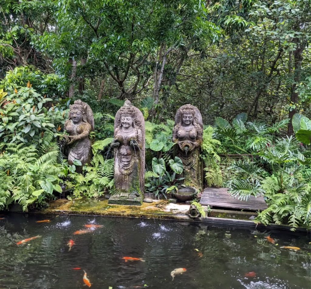Stone Balinese statues by a koi pond surrounded by lush greenery