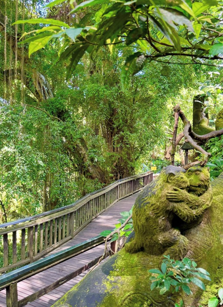 Moss-covered monkey statue on a wooden path in Bali's lush jungle.