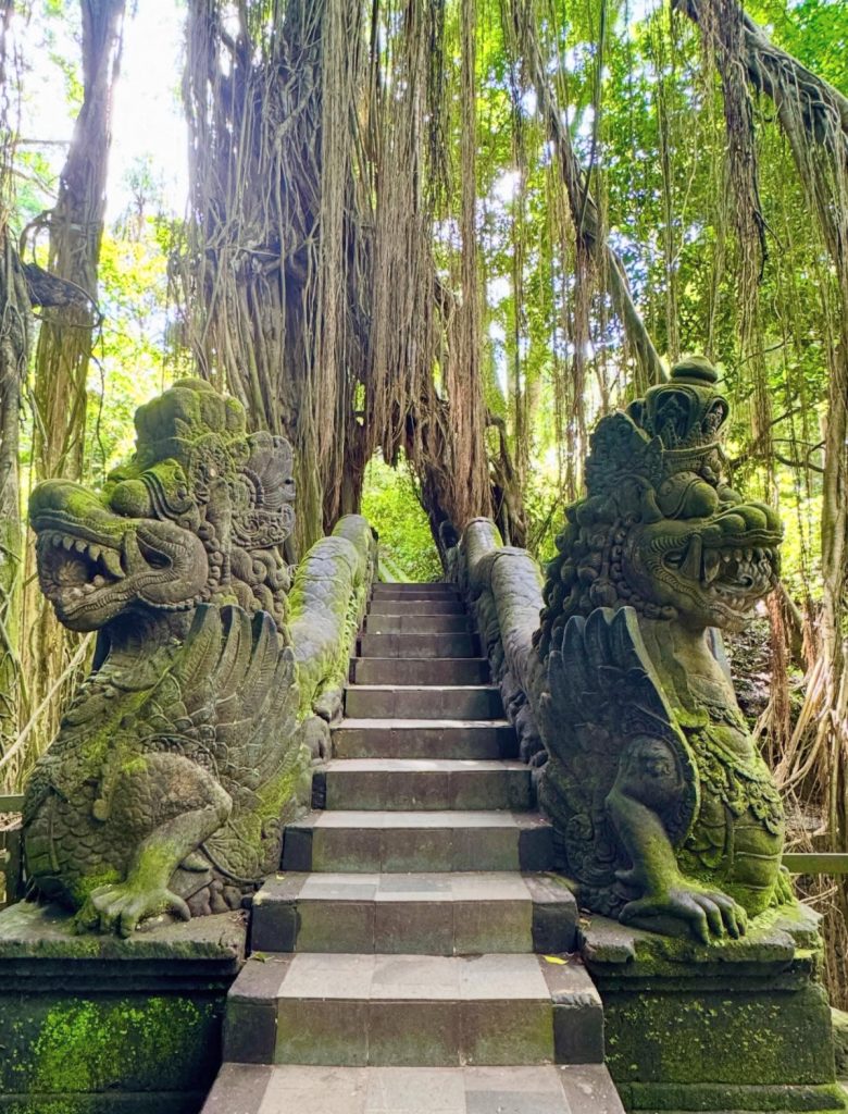 Ancient stone dragon statues guard moss-covered stairs in a Bali jungle.