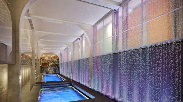 Cruise ship spa with pools and illuminated water feature wall.