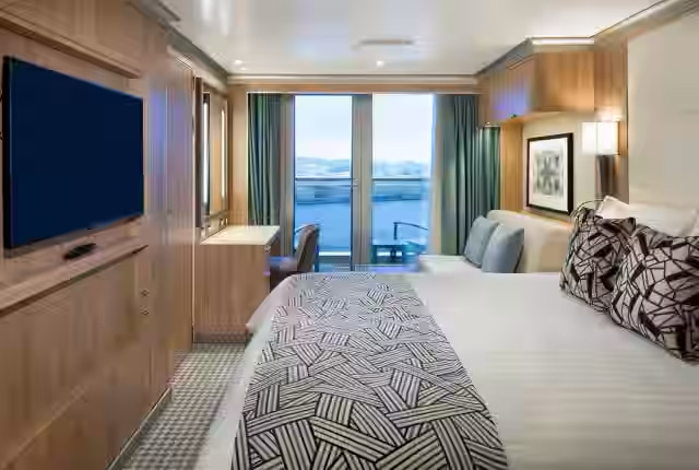 Cruise ship cabin with balcony, bed, and desk.