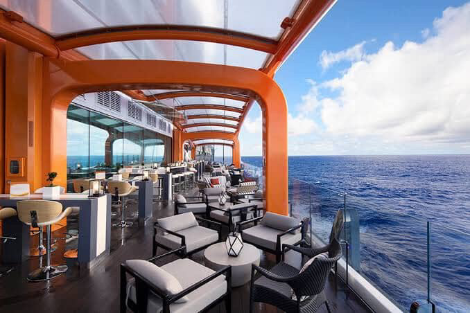 Outdoor lounge on a cruise ship with orange accents, chairs, and ocean view.
