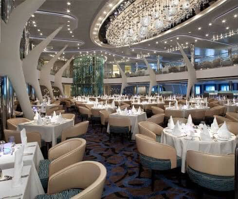 Elegant dining room on a cruise ship with chandelier and tables.