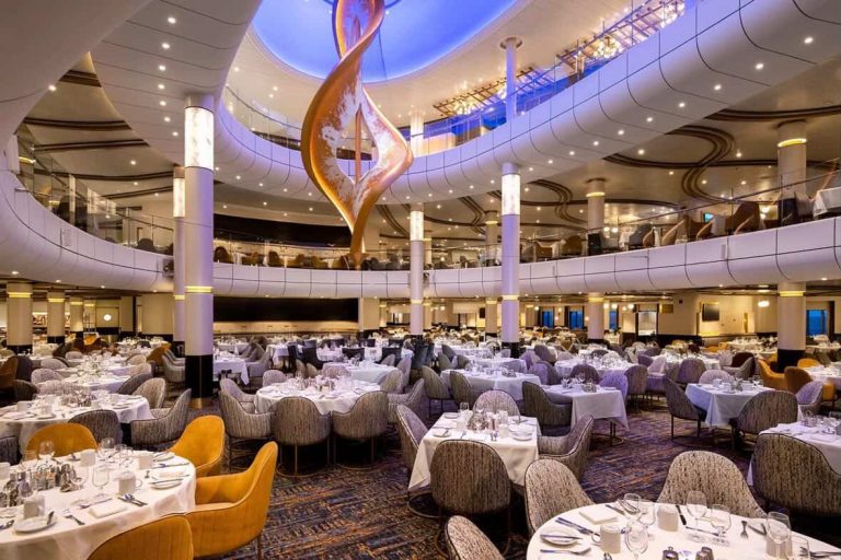 Elegant main dining room on a cruise ship with tables set and a multi-story atrium.