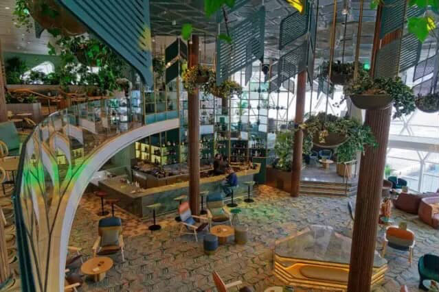Cruise ship bar with lush greenery and spiral staircase.