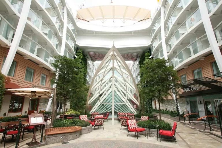 Cruise ship's Central Park with greenery, seating, and glass structure.