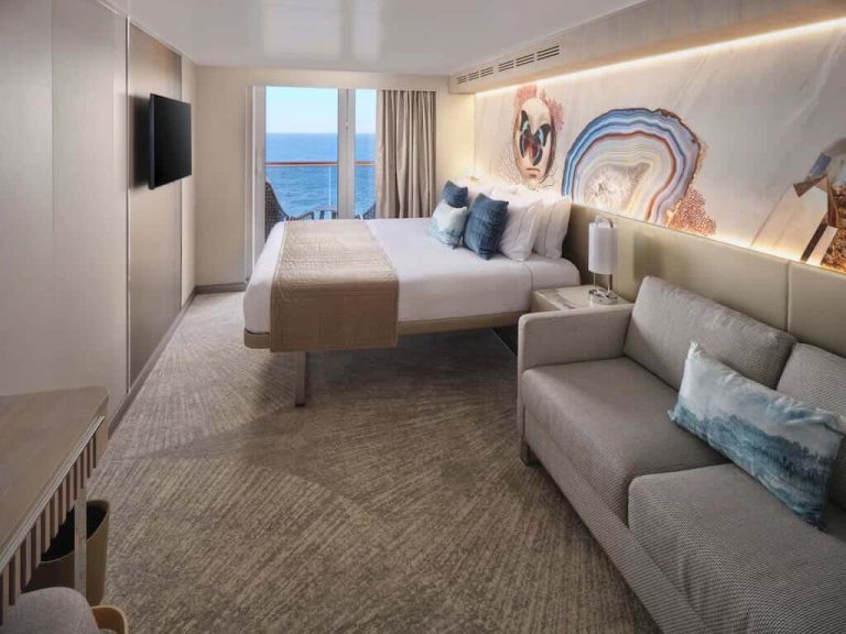 Cruise ship stateroom with balcony and ocean view, featuring a king-size bed and sofa.