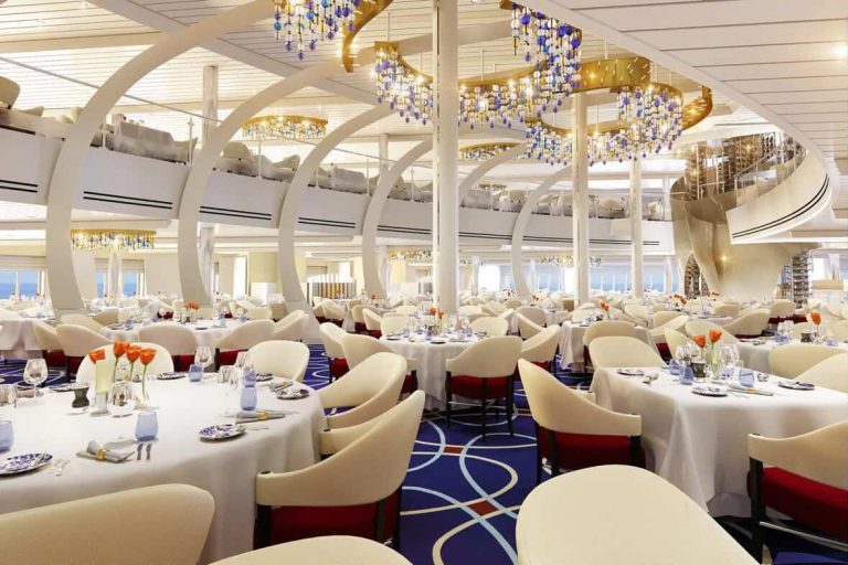 Elegant cruise ship dining room with chandeliers and spiral staircase.
