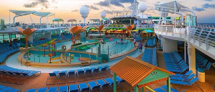 Cruise ship pool deck with lounge chairs and water park features.