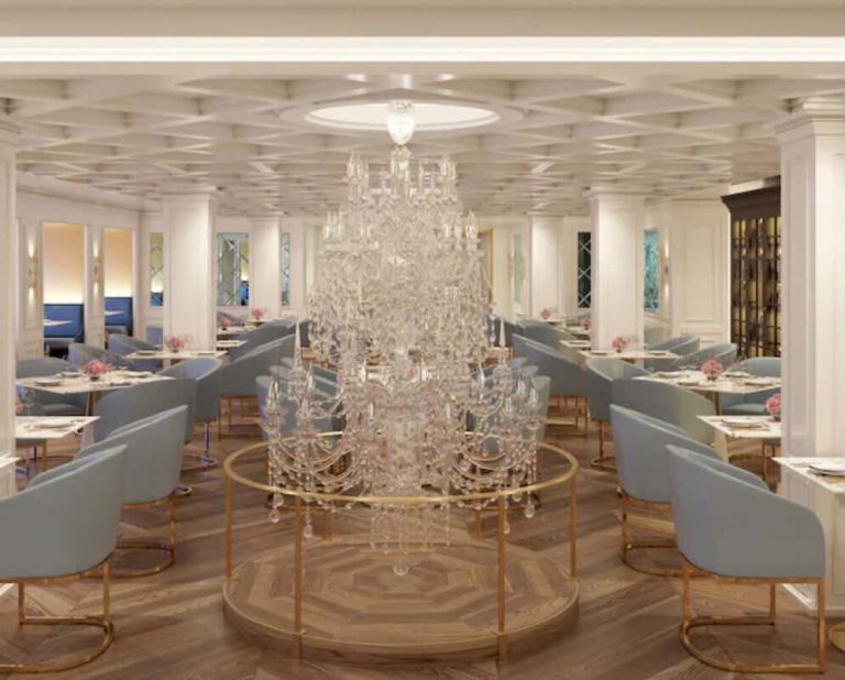 Elegant cruise ship dining room with chandelier, tables, and blue chairs.