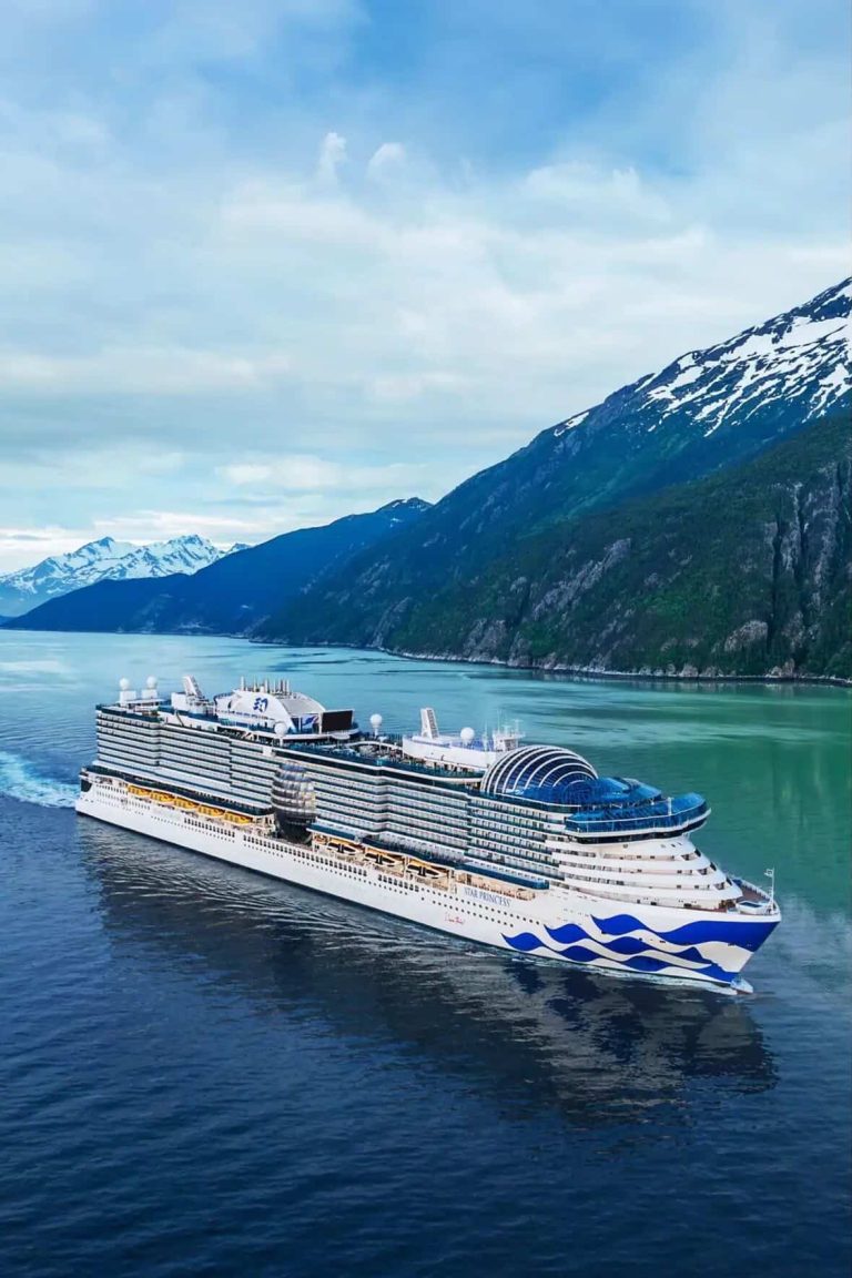 Cruise ship sailing through Alaskan waters with snow-capped mountains in the background.