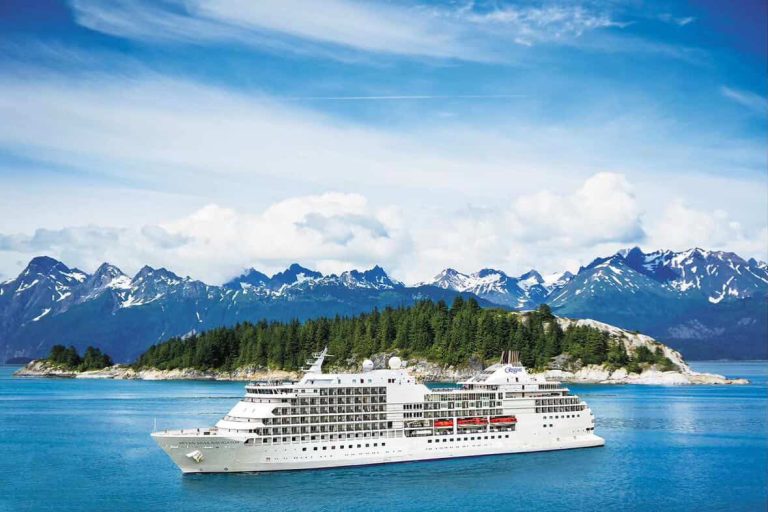 Cruise ship sailing through Alaskan waters with mountains in the background.