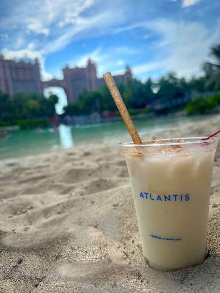 Atlantis drink on beach with resort in background. Text: ATLANTIS, Commercially Compostable.