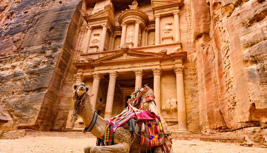 Camel rests in front of Al-Khazneh (The Treasury) at Petra, Jordan. Ancient sandstone architecture.