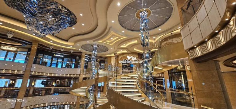 Cruise ship atrium with grand staircase and chandeliers.