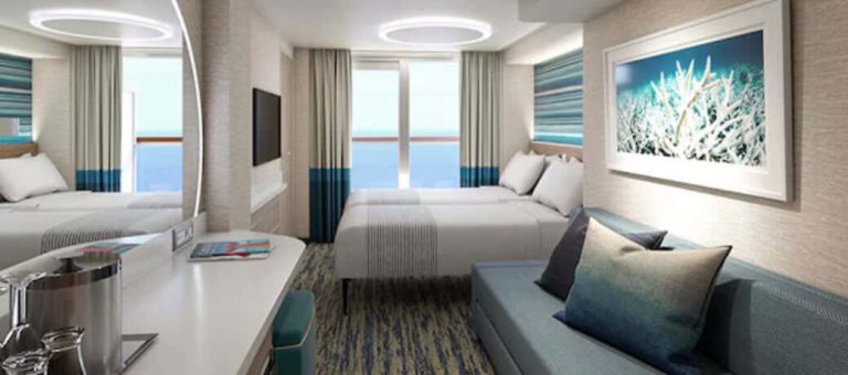 Cruise ship balcony stateroom with beds, sofa, and ocean view.