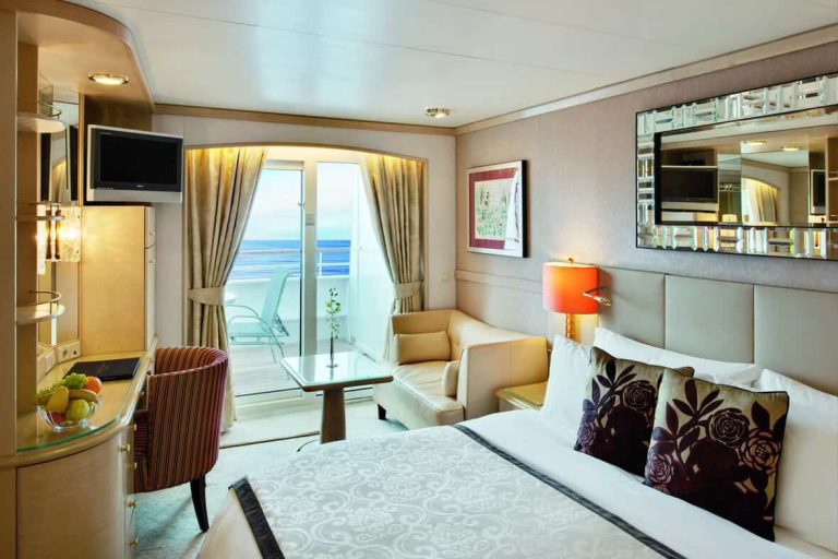 Cruise ship cabin with balcony, bed, seating area, and ocean view. Luxurious cruise interior.