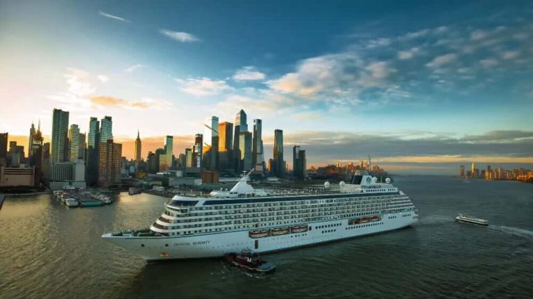 Cruise ship in harbor with city skyline backdrop at sunset.