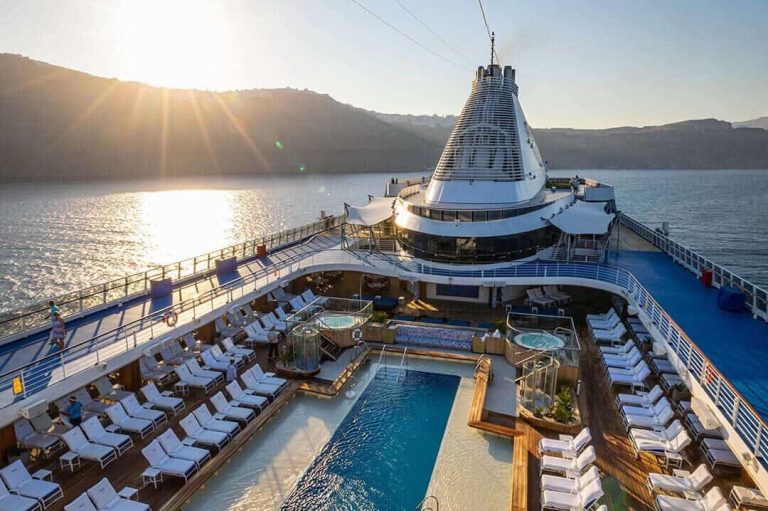 Cruise ship deck with pool, sun loungers, and ocean view at sunset.